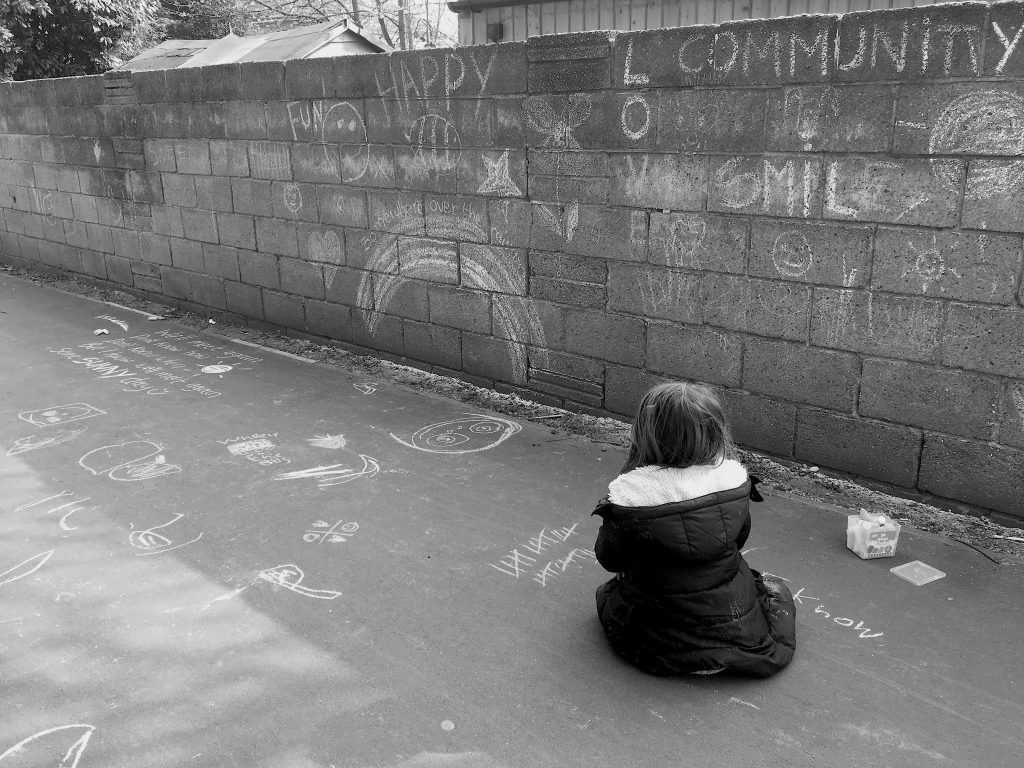 One year on. Child sat down looking at a wall illustrated with chalk writing and drawings.